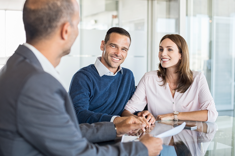 A male mortgage adviser offers financial advice to a man and a woman. The couple are both smiling at the financial adviser.